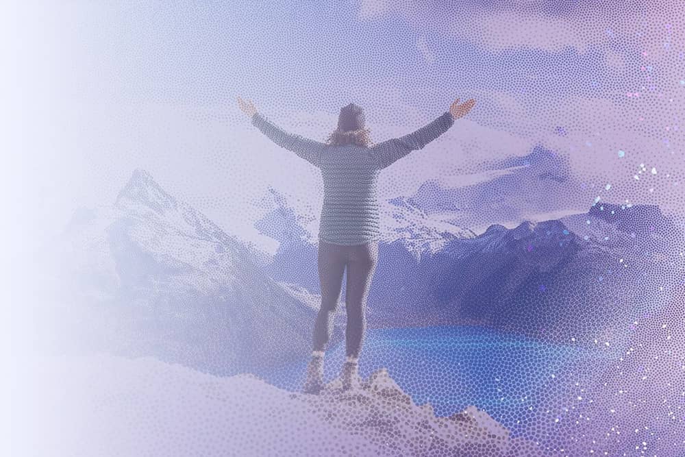 Woman standing on top of mountain with her arms in the air overlooking another mountain range