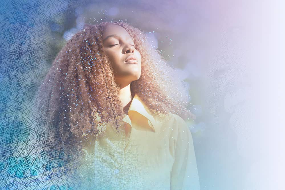 Woman with her hair out and her face in the sun with nature in the background